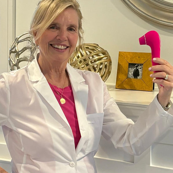 VIVA Nurse Maureen holding a pink intimate pleasure product in a white lab coat, with decorative items in the background.