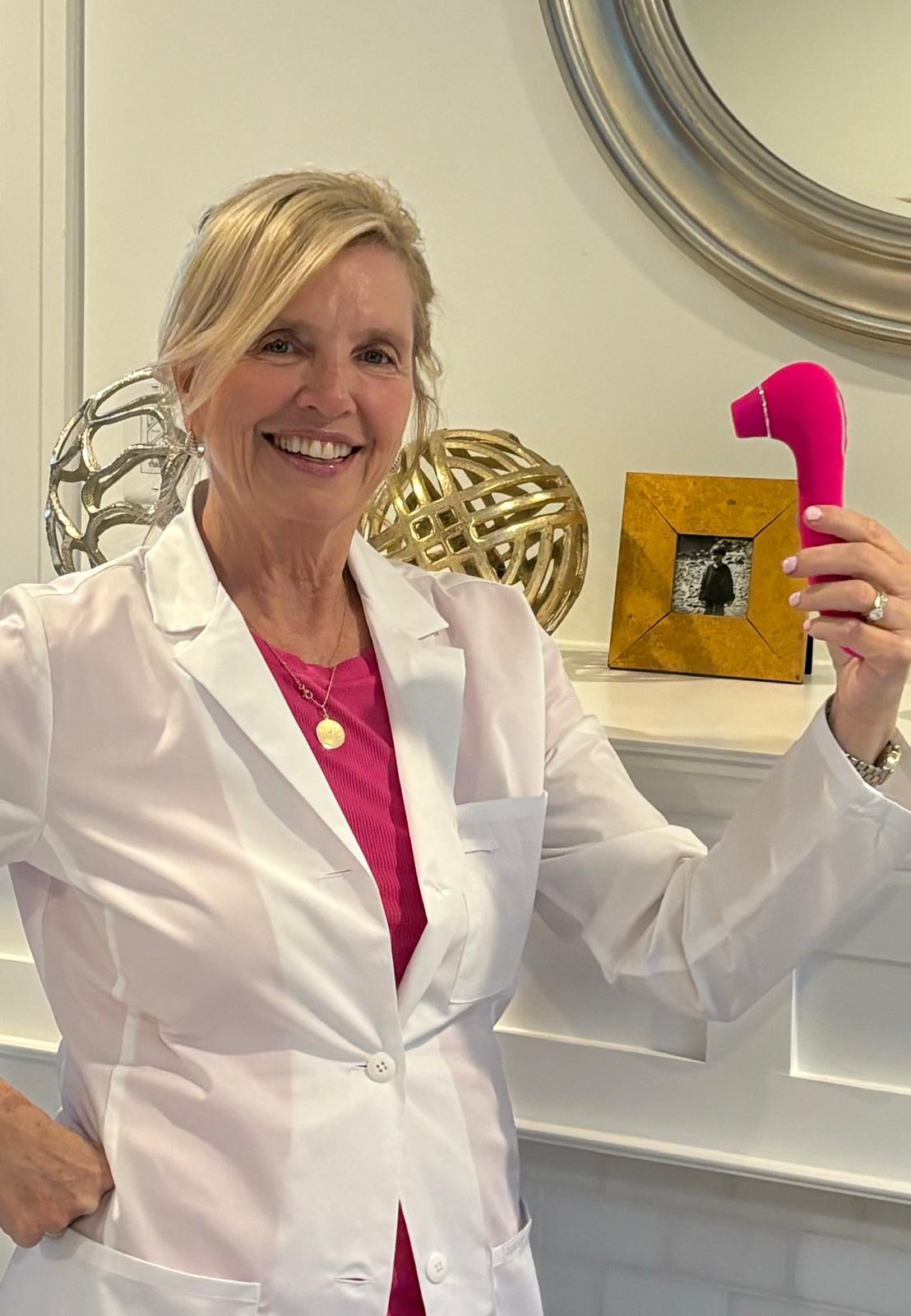 VIVA Nurse Maureen holding a pink intimate pleasure product in a white lab coat, with decorative items in the background.